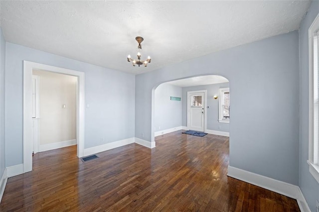 interior space featuring arched walkways, a notable chandelier, dark wood-style flooring, visible vents, and baseboards