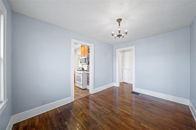 empty room featuring a chandelier, baseboards, visible vents, and hardwood / wood-style floors