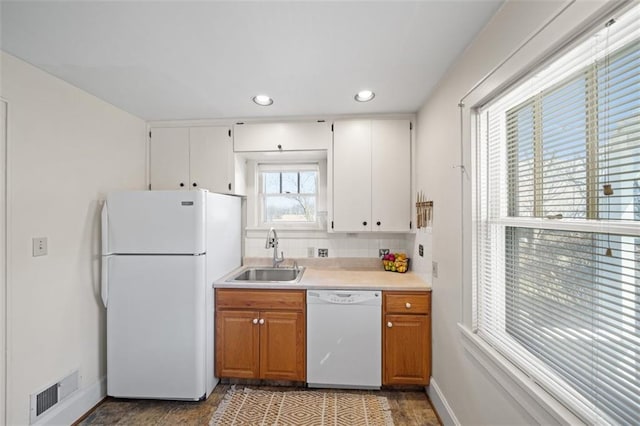 kitchen with white appliances, a sink, visible vents, white cabinetry, and light countertops