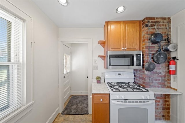 kitchen featuring white range with gas stovetop, light countertops, open shelves, stainless steel microwave, and plenty of natural light