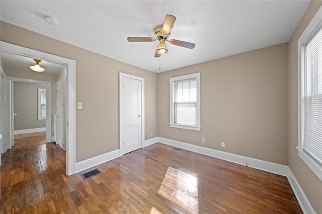 empty room with dark wood-type flooring, visible vents, ceiling fan, and baseboards