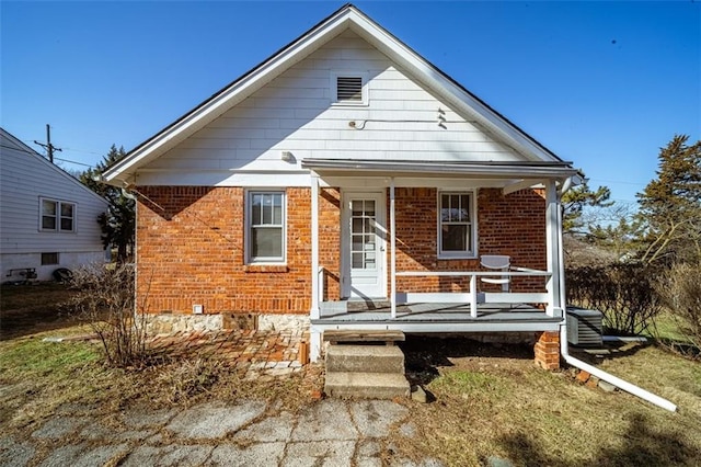 bungalow featuring covered porch, brick siding, and central AC