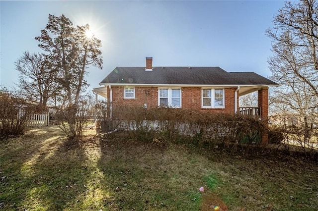 back of house with a chimney, a lawn, and brick siding