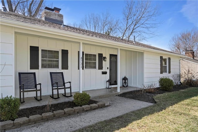 property entrance featuring a lawn, a porch, a chimney, and board and batten siding