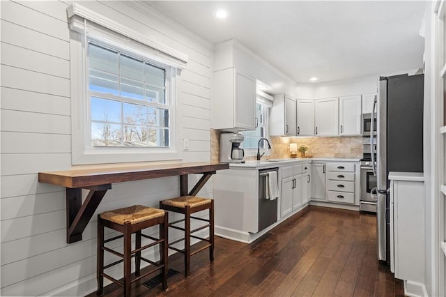 kitchen with dark wood-style flooring, stainless steel appliances, light countertops, white cabinetry, and tasteful backsplash