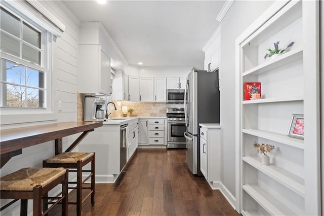 kitchen with crown molding, appliances with stainless steel finishes, dark wood-style floors, white cabinets, and a sink