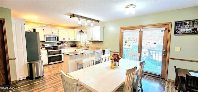 kitchen featuring white cabinetry, hanging light fixtures, a kitchen breakfast bar, hardwood / wood-style flooring, and stainless steel appliances