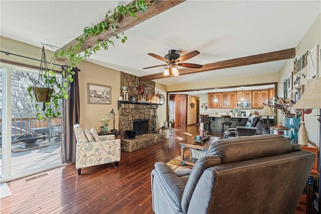 living room with ceiling fan, a stone fireplace, dark hardwood / wood-style floors, and beam ceiling