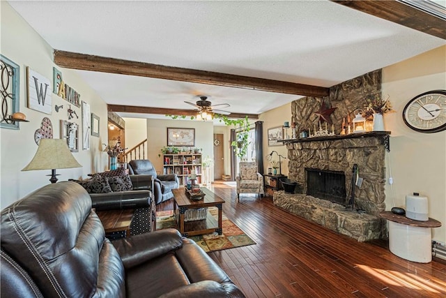 living room with beamed ceiling, ceiling fan, a stone fireplace, and dark hardwood / wood-style flooring