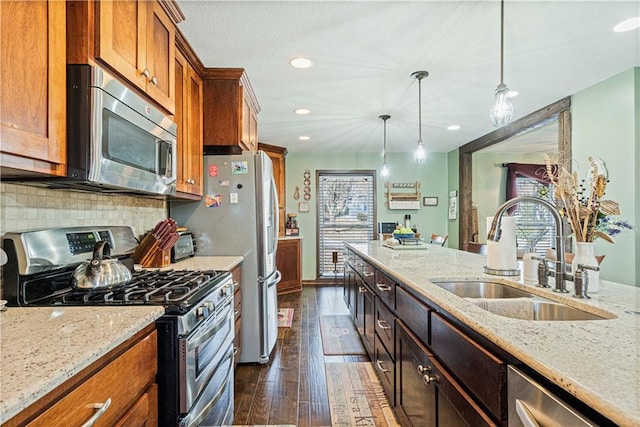 kitchen featuring light stone counters, sink, decorative light fixtures, and stainless steel appliances