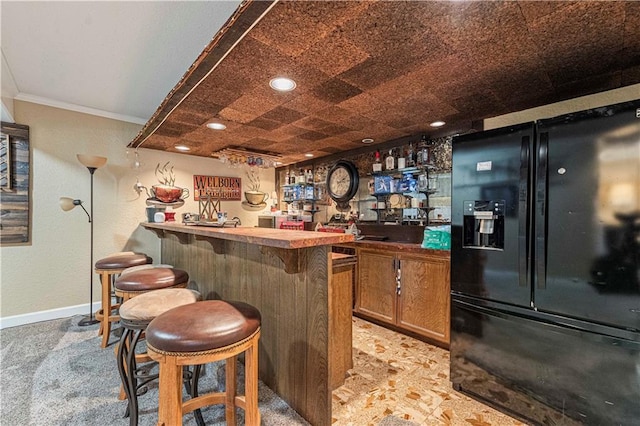 bar featuring crown molding and black refrigerator with ice dispenser