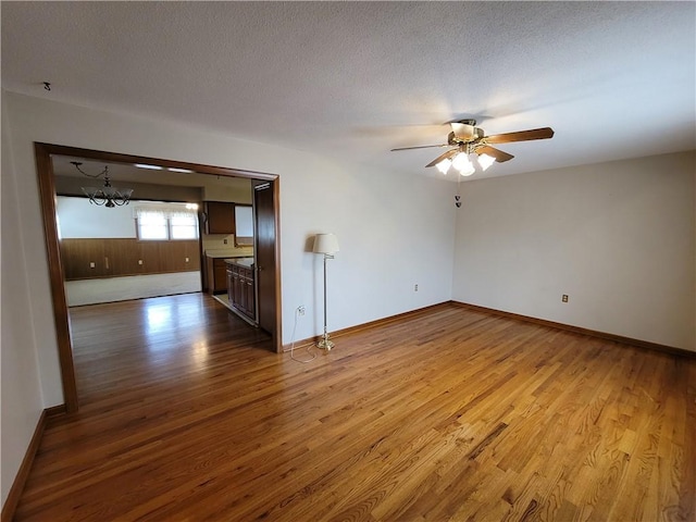 unfurnished living room featuring ceiling fan with notable chandelier, light hardwood / wood-style floors, and a textured ceiling