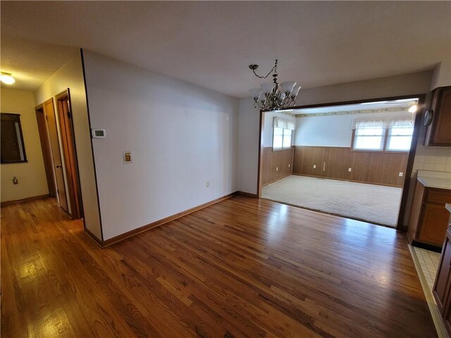 unfurnished dining area featuring wood walls, wood-type flooring, and a notable chandelier