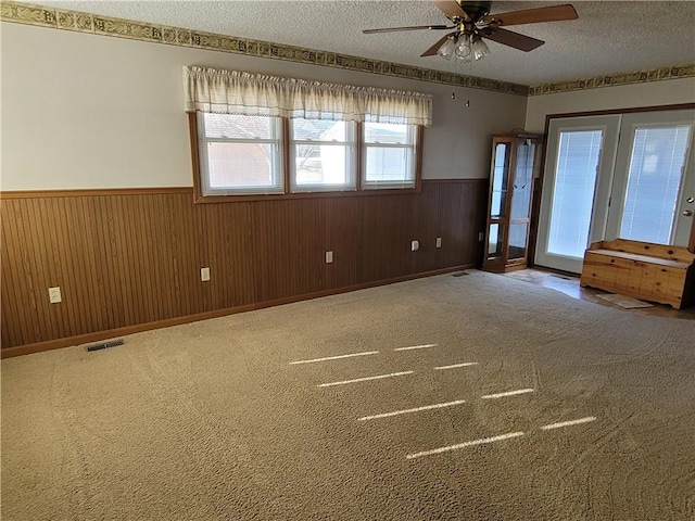 carpeted empty room with ceiling fan, french doors, a textured ceiling, and wood walls