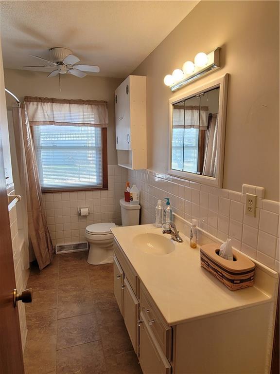 bathroom featuring ceiling fan, vanity, toilet, and tile walls