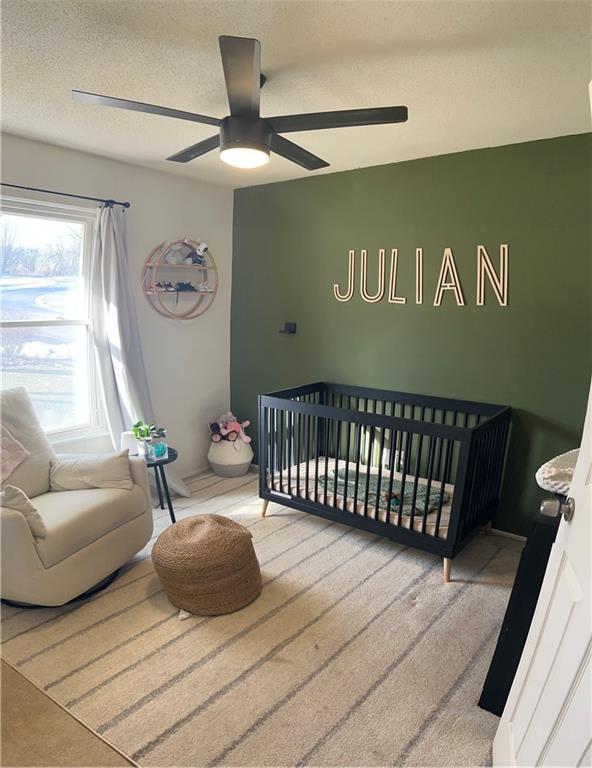 bedroom with ceiling fan, a nursery area, and a textured ceiling