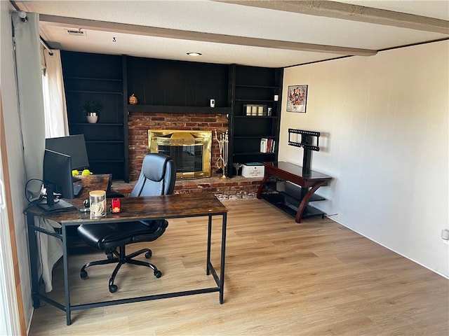 home office with a fireplace, beam ceiling, and light hardwood / wood-style flooring