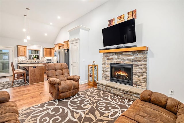 living room with a stone fireplace, vaulted ceiling, and light hardwood / wood-style flooring