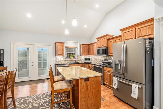 kitchen featuring french doors, hanging light fixtures, a kitchen island, stainless steel appliances, and light stone countertops