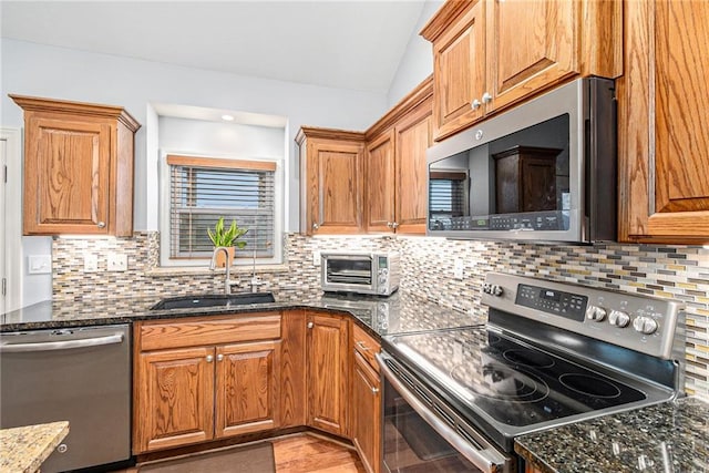 kitchen with sink, dark stone countertops, stainless steel appliances, tasteful backsplash, and vaulted ceiling