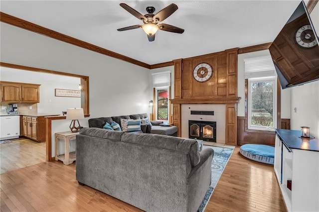 living area featuring ceiling fan, ornamental molding, a tile fireplace, and light wood-style floors