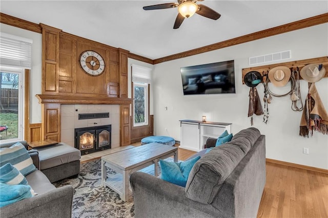 living room featuring visible vents, a tile fireplace, ceiling fan, crown molding, and light wood-type flooring