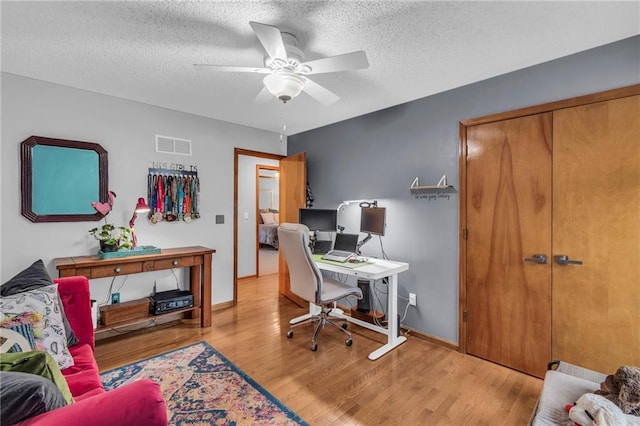 office space with a textured ceiling, ceiling fan, wood finished floors, visible vents, and baseboards