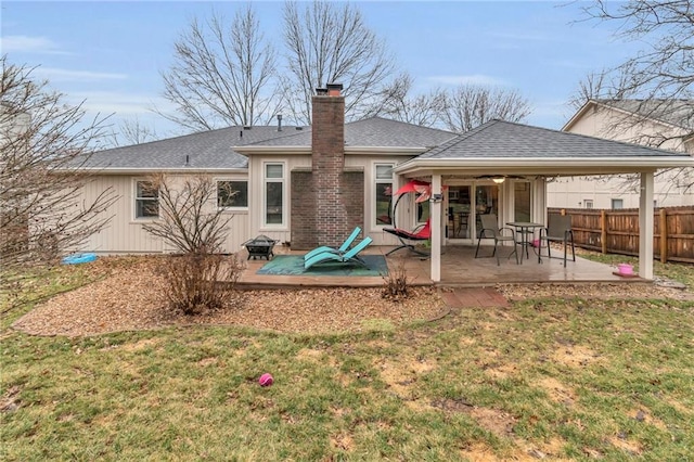 rear view of property featuring roof with shingles, a yard, a chimney, a patio, and fence