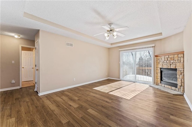 unfurnished living room with dark hardwood / wood-style floors, a tray ceiling, a stone fireplace, and a textured ceiling