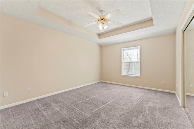 carpeted empty room with ceiling fan, a raised ceiling, and a textured ceiling