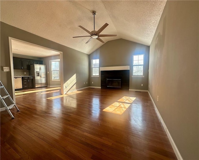 unfurnished living room with dark wood-type flooring, ceiling fan, lofted ceiling, and a textured ceiling