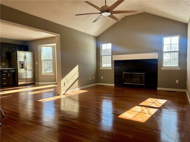 unfurnished living room featuring plenty of natural light, dark hardwood / wood-style floors, a textured ceiling, and vaulted ceiling