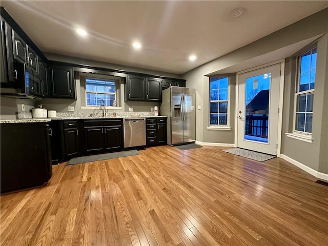 kitchen with light stone counters, sink, light hardwood / wood-style flooring, and appliances with stainless steel finishes