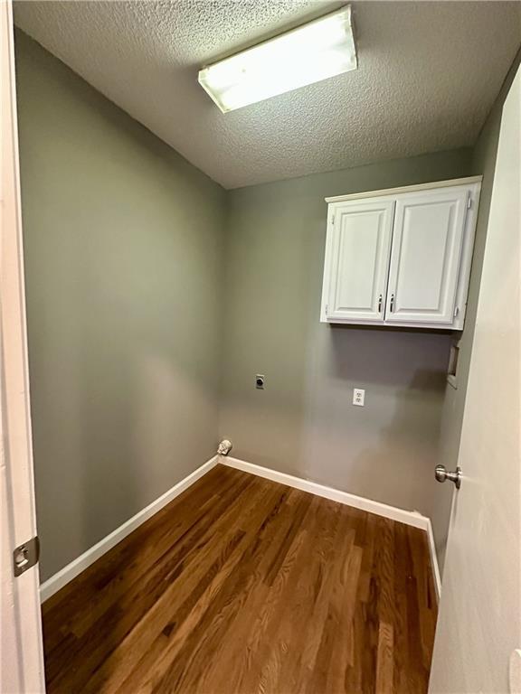 washroom with cabinets, electric dryer hookup, hardwood / wood-style flooring, and a textured ceiling