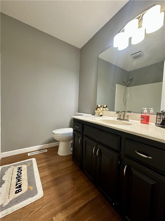 bathroom featuring toilet, a shower, a textured ceiling, vanity, and hardwood / wood-style floors