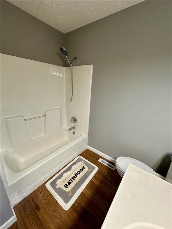 bathroom featuring toilet, shower / bath combination, hardwood / wood-style floors, and a textured ceiling