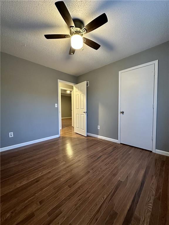 unfurnished bedroom featuring ceiling fan, dark hardwood / wood-style floors, and a textured ceiling