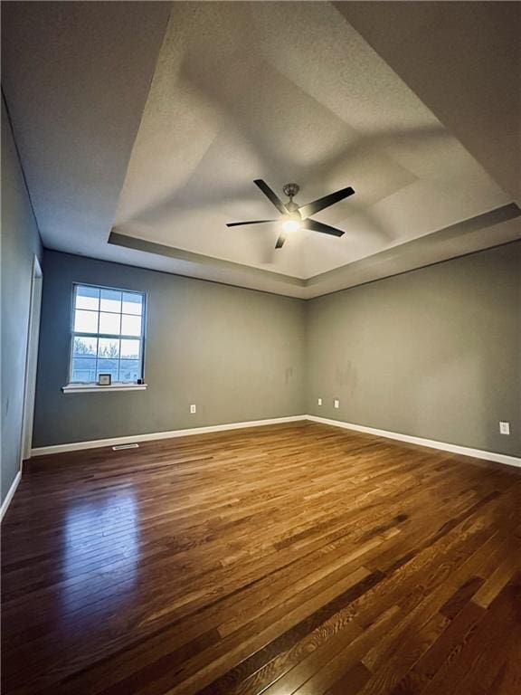 empty room featuring a raised ceiling, hardwood / wood-style flooring, a textured ceiling, and ceiling fan