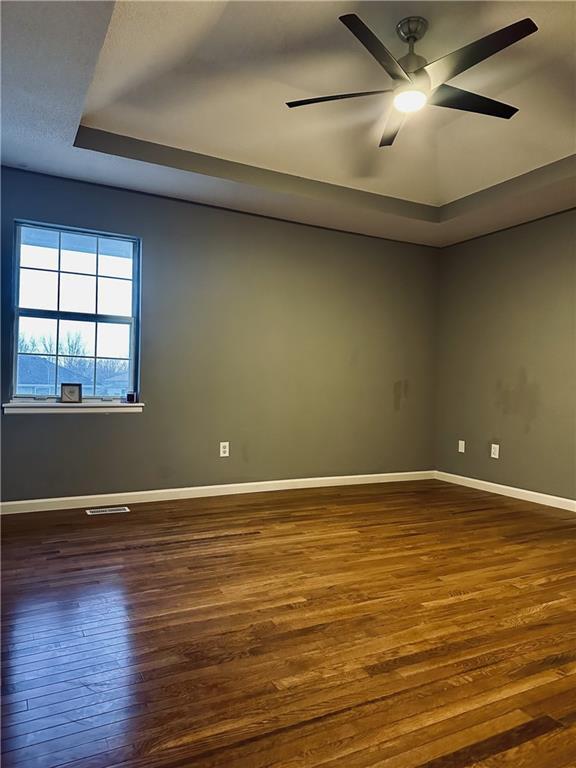 empty room with dark hardwood / wood-style floors, a raised ceiling, and ceiling fan