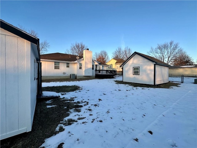 snowy yard featuring central AC unit, an outbuilding, and a deck