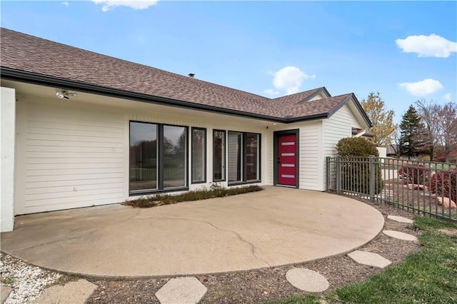 rear view of property with roof with shingles, a patio, and fence