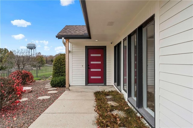 view of exterior entry featuring a shingled roof and fence