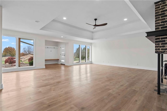 unfurnished living room with baseboards, ceiling fan, a tray ceiling, and wood finished floors