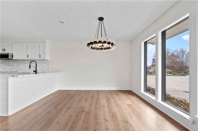 unfurnished dining area with light wood finished floors, baseboards, a chandelier, and a sink