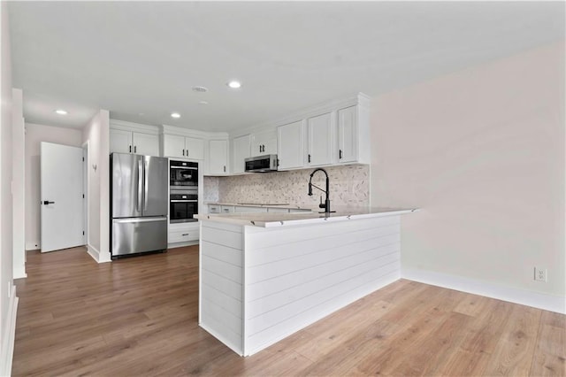 kitchen featuring stainless steel appliances, a peninsula, a sink, light wood-type flooring, and decorative backsplash