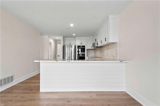 kitchen featuring stainless steel appliances, tasteful backsplash, visible vents, light wood-style flooring, and a peninsula