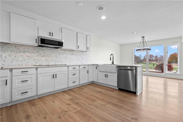 kitchen featuring stainless steel appliances, a peninsula, a sink, white cabinetry, and light wood-style floors