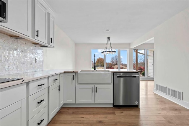 kitchen featuring light wood finished floors, stainless steel appliances, light countertops, a sink, and a peninsula