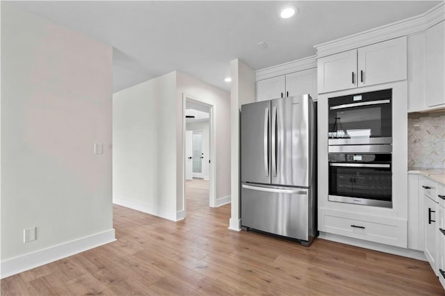 kitchen with light wood finished floors, baseboards, decorative backsplash, appliances with stainless steel finishes, and white cabinetry