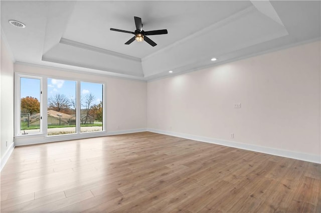 empty room featuring baseboards, a raised ceiling, ceiling fan, light wood-style flooring, and ornamental molding